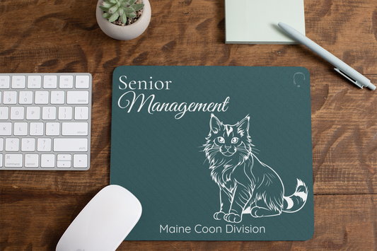 Senior Management - Maine Coon Division mousepad featuring white line art of a majestic Maine Coon cat on forest green background, displayed on wooden desk with keyboard, mouse, succulent plant and pen