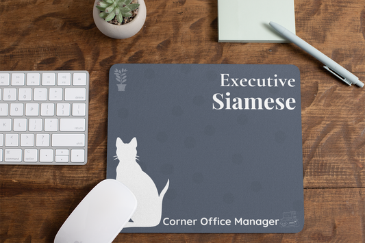 Executive Siamese - Corner Office Manager Mousepad featuring a white Siamese cat silhouette on slate blue background with polka dots, displayed on wooden desk with keyboard, succulent plant, and pen, perfect for home office setup.