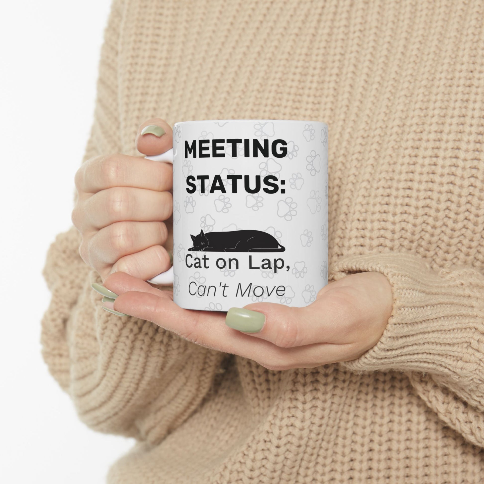 White ceramic mug with "Meeting Status: Cat on Lap, Can't Move" text and black cat silhouette design, shown held by hands wearing beige sweater, featuring "Cat on Lap" Meeting Status design for remote workers with feline supervisors