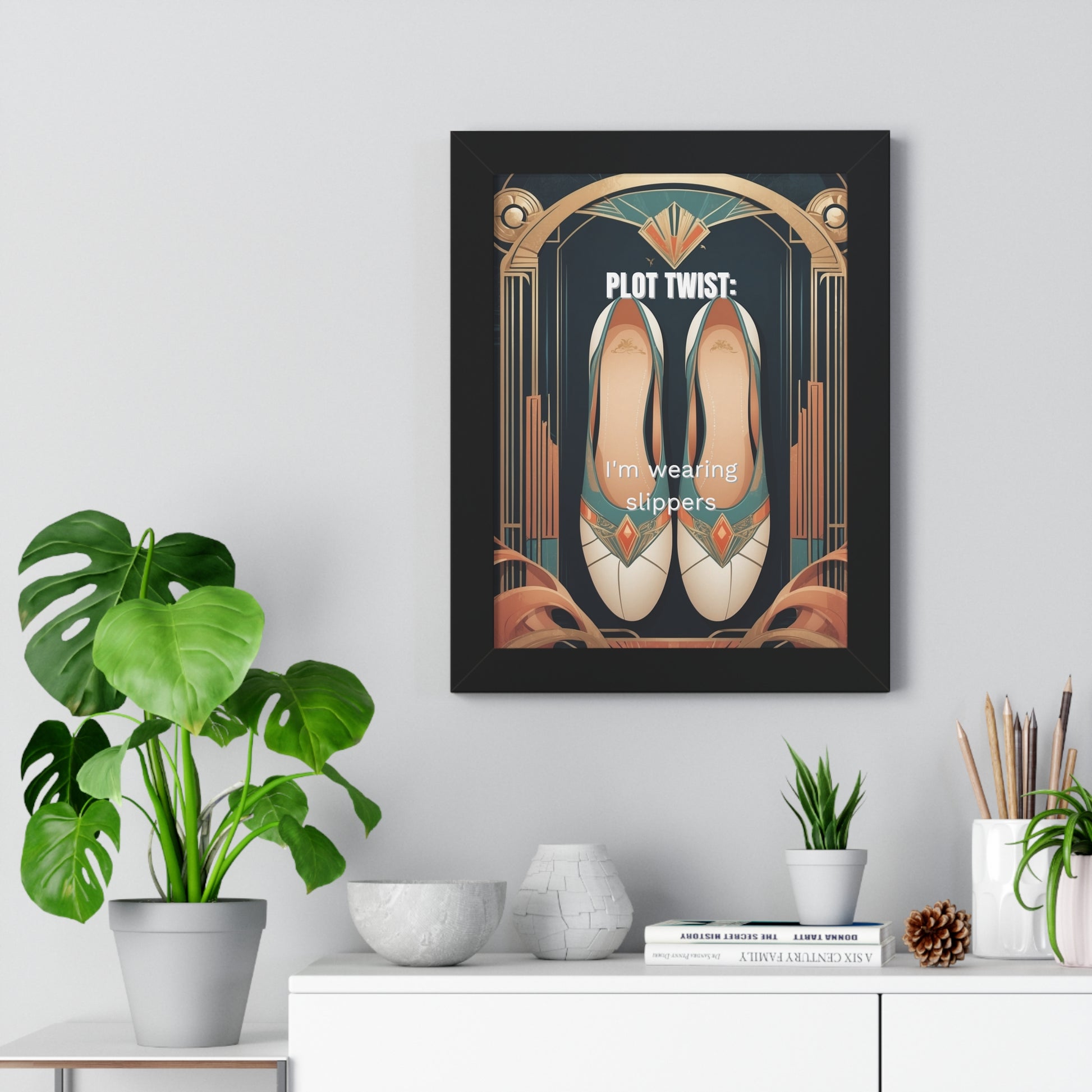 Art Deco framed print 'Plot Twist: I'm Wearing Slippers' featuring elegant beige ballet slippers within ornate gold geometric archway design against navy background. Black frame mounted on light gray wall with decorative plants. Modern home office wall decor with humorous work-from-home message.